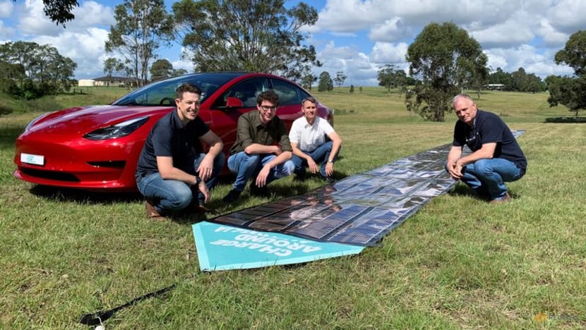 2022年4月10日，在澳大利亚戈斯福斯，参与澳大利亚周边充电项目的团队在打印的太阳能板和特斯拉汽车附近拍照。
